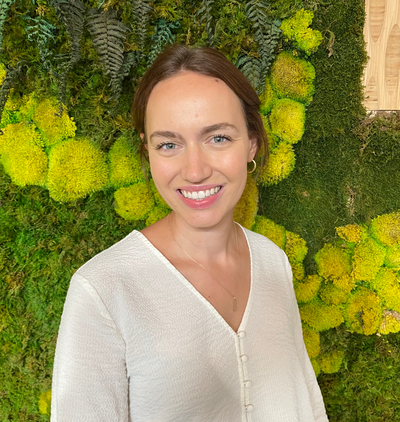 Headshot of Anna Hilke smiling in front of a wall covered in green plants.