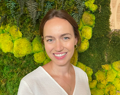Headshot of Anna Hilke, smiling in a white shirt with a green moss background.