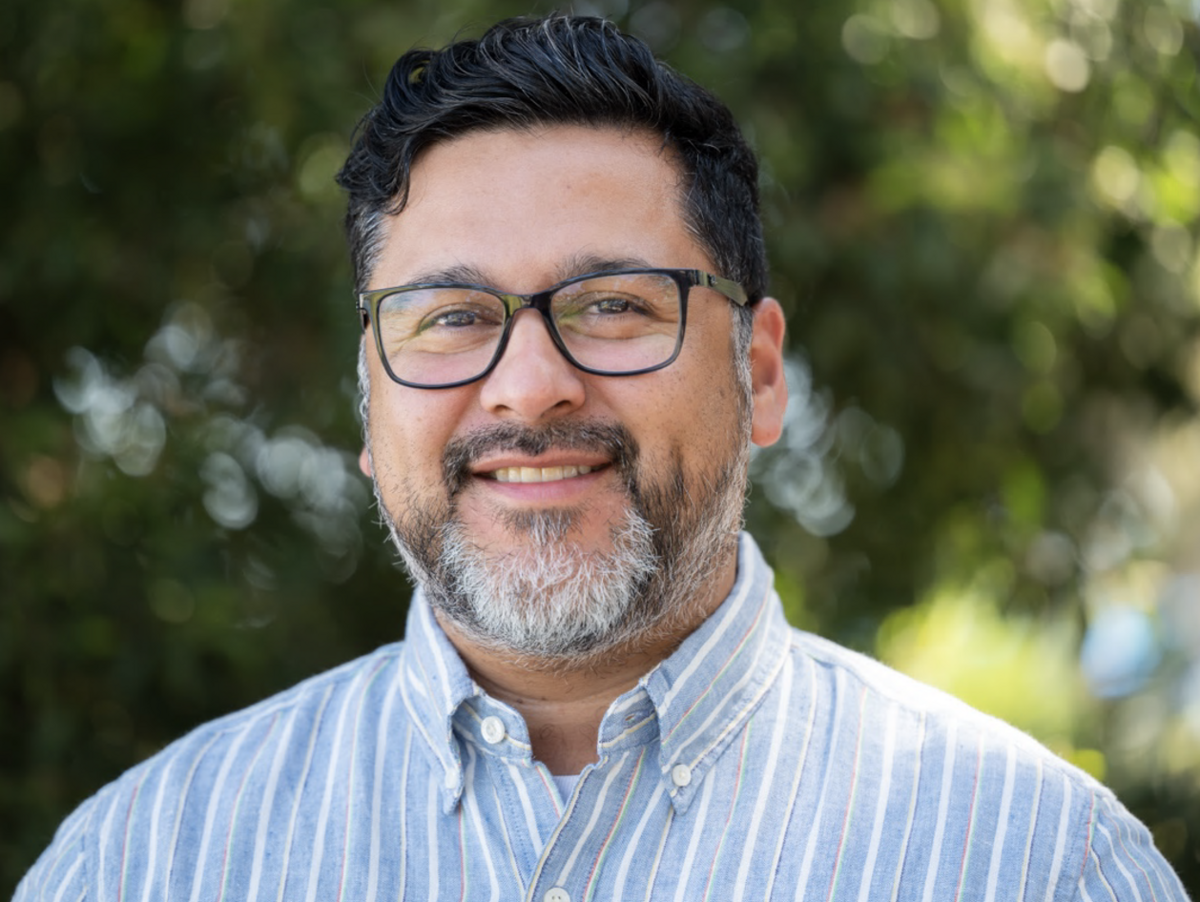 Headshot of Julio Gomez smiling in front of green trees.