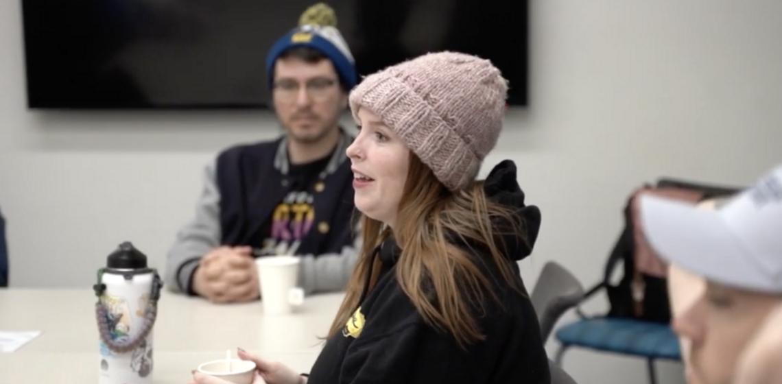 A re-entry student and OWLs attendee in a pink knit hat and black hoodie holds a cup, smiling in discussion.