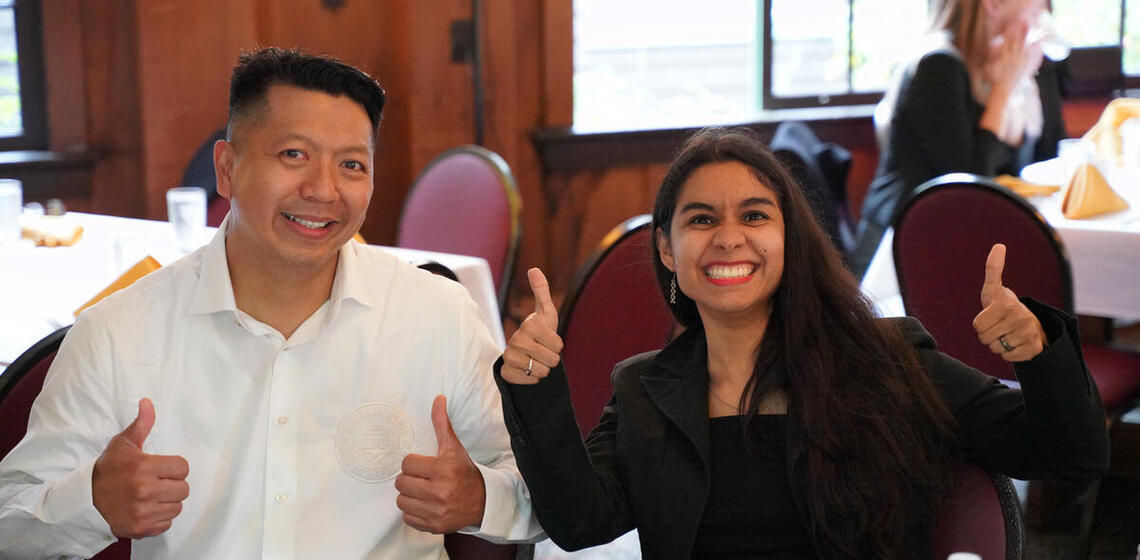 two students at a re-entry student event smiling and giving a thumbs up to the camera