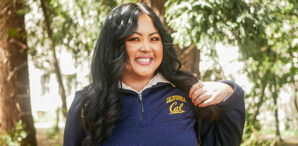 student smiling and wearing cal sweater gesturing at berkeley logo
